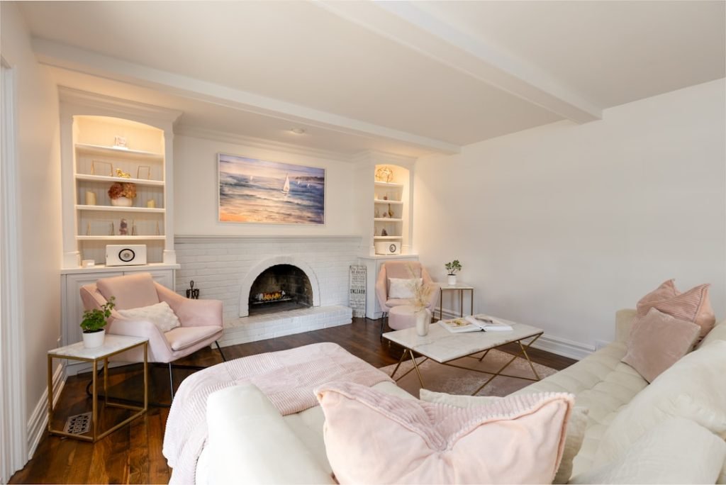 A bright, cozy living room with blush tones, gold accents, and a white brick fireplace, styled for calm and comfort.