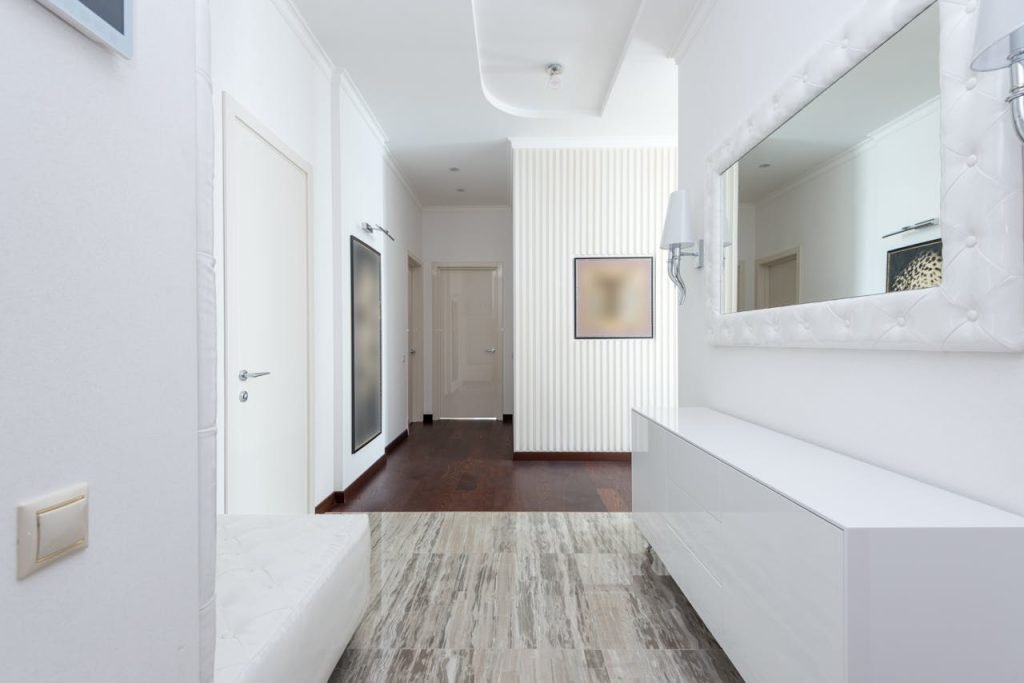 Bright corridor with contemporary design featuring white walls, minimal decor, and mirror.